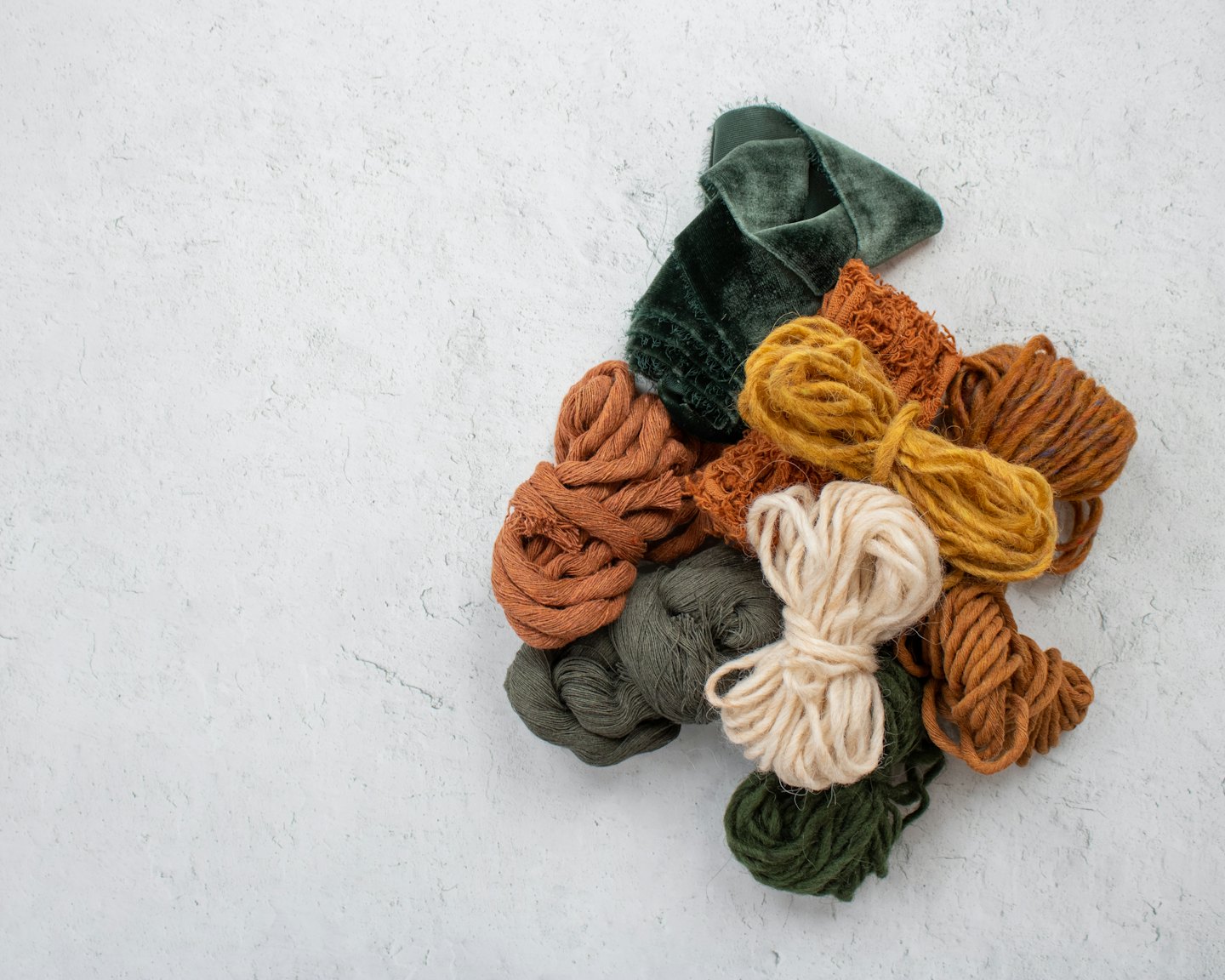 Assorted earthy toned yarns and fabrics laid out on a textured surface.