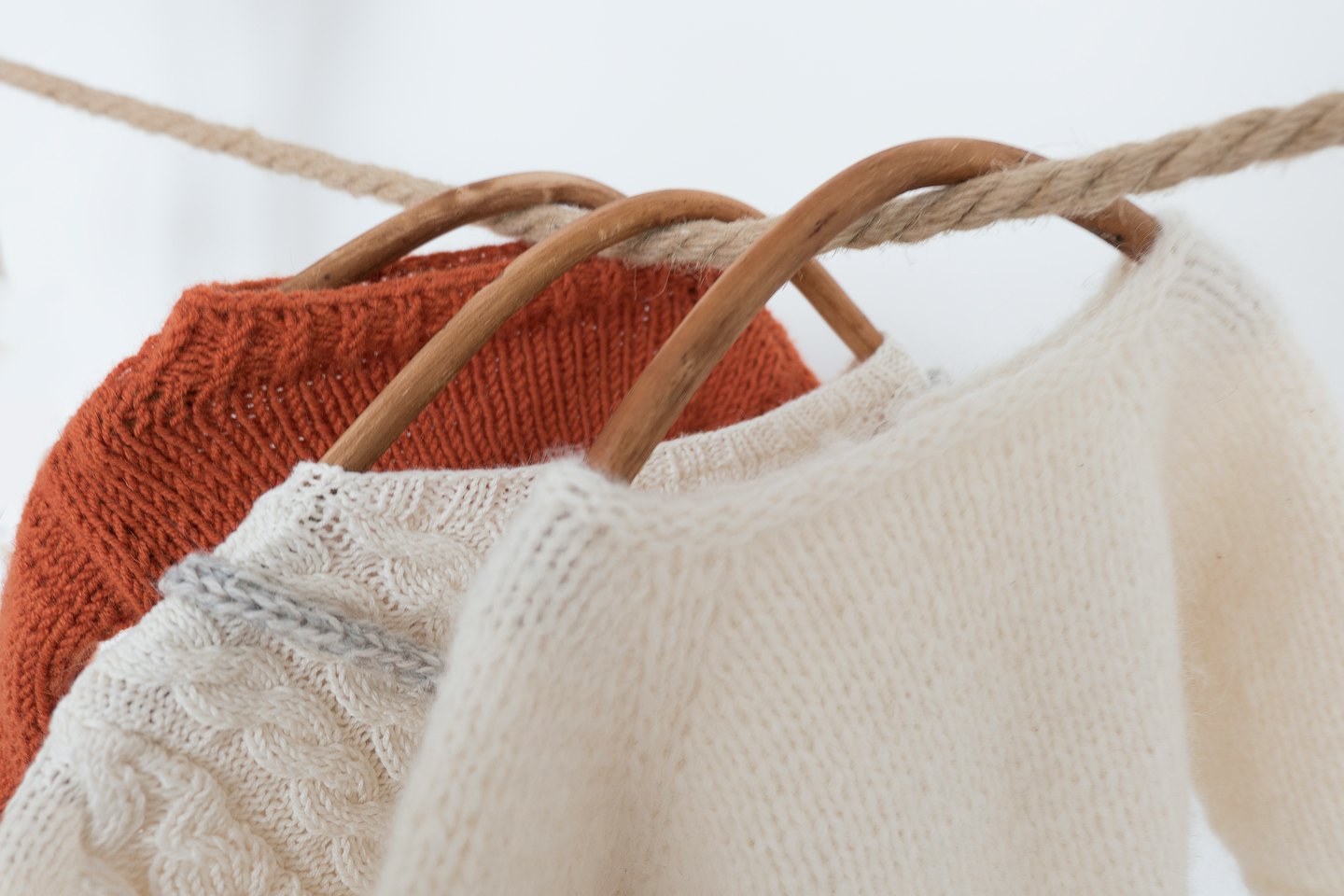Three knitted sweaters hang on wooden hangers from a rope.