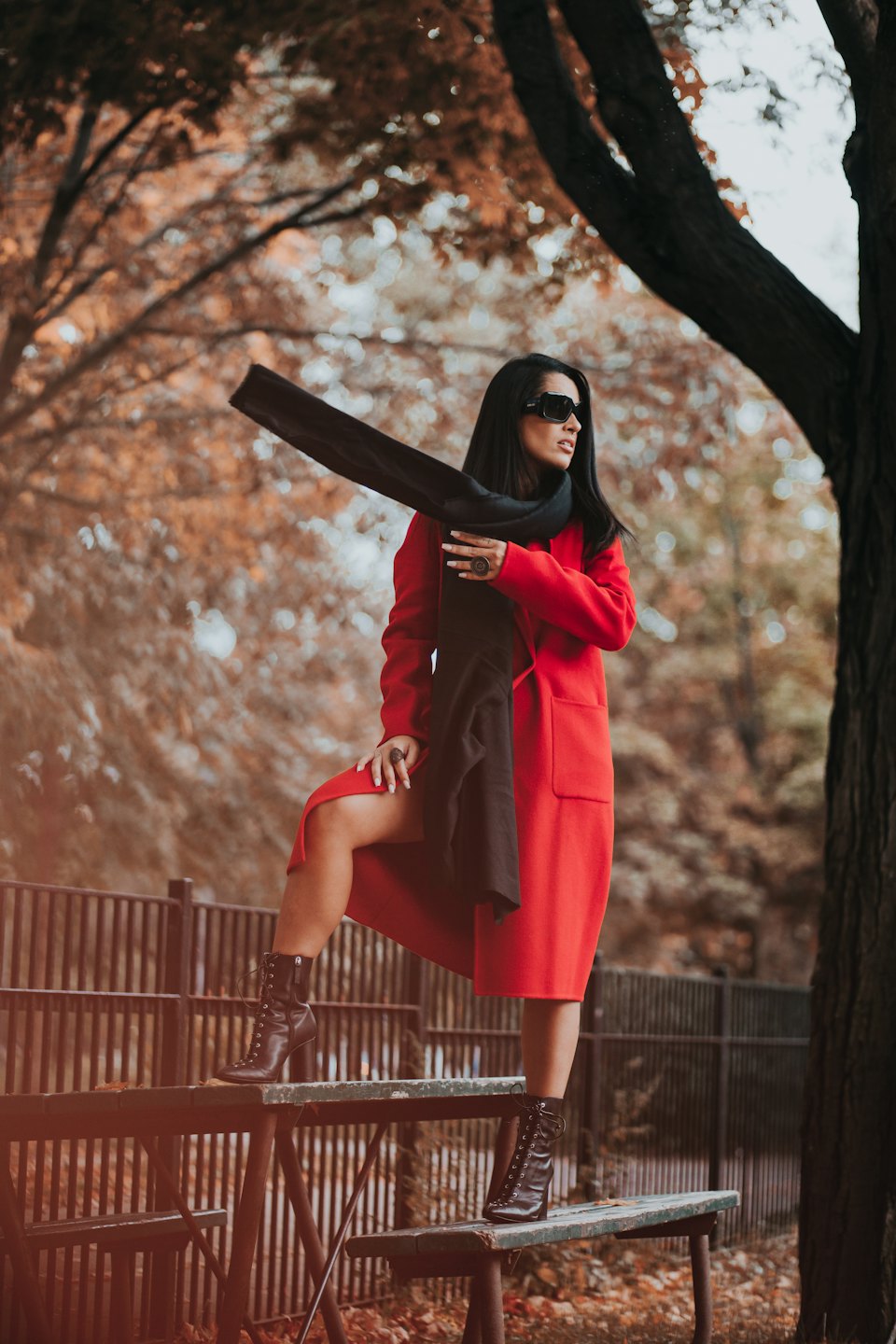 Woman in red coat poses on a wooden bench among autumn trees.