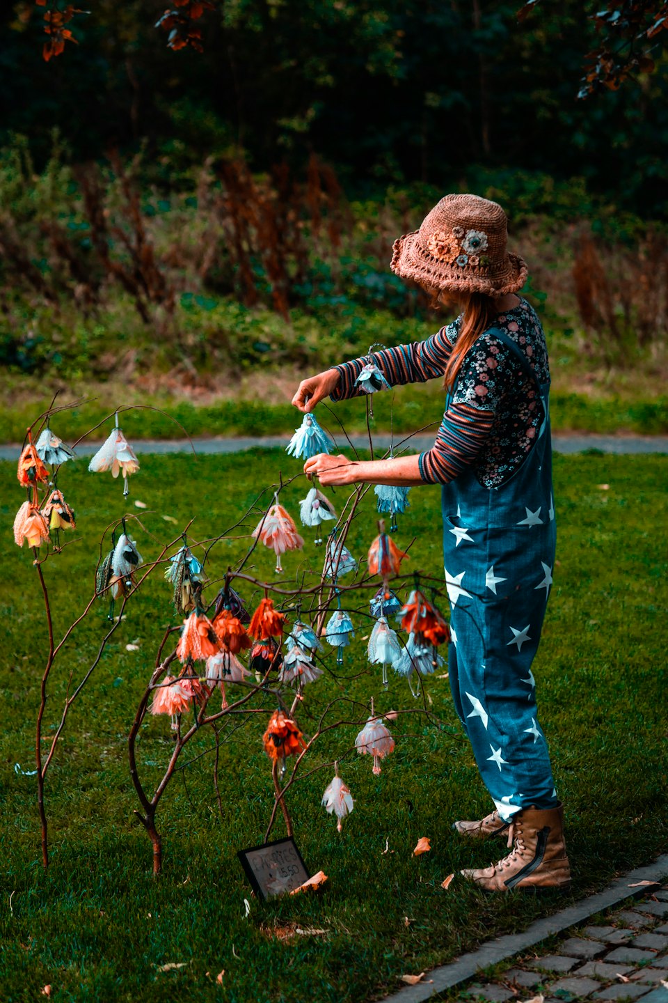 Person in overalls hanging bead ornaments on a garden branch.